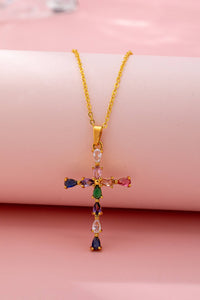 Gold cross necklace with colorful gemstones on a pink background