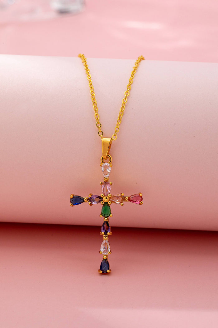 Gold cross necklace with colorful gemstones on a pink background