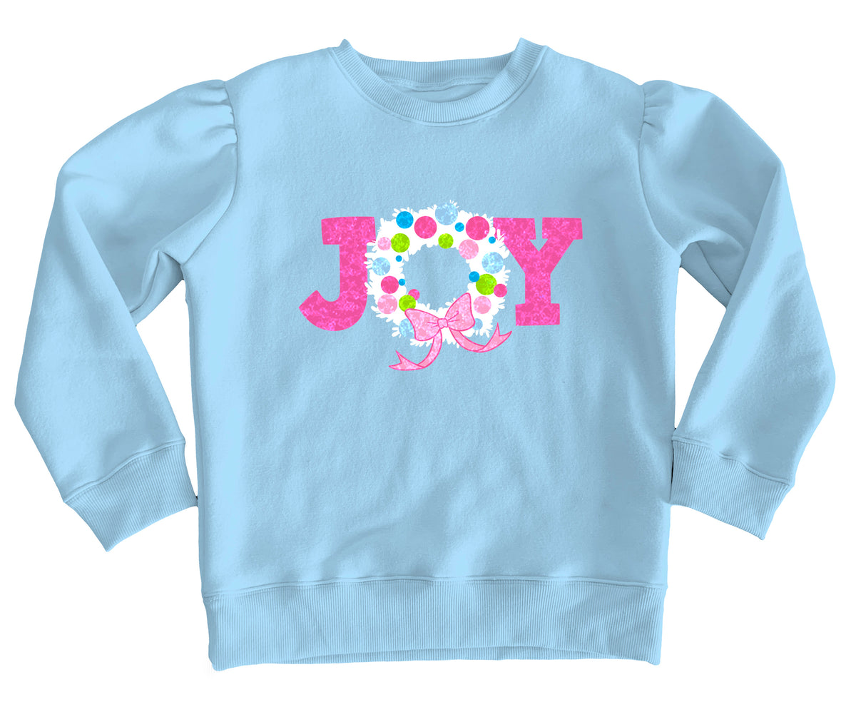 A light blue long-sleeve sweatshirt with a pink and white 'JOY' graphic on the chest, featuring a floral wreath design inside the 'O' and a pink bow.