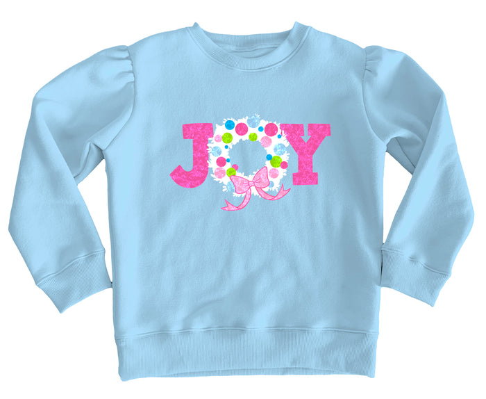 A light blue long-sleeve sweatshirt with a pink and white 'JOY' graphic on the chest, featuring a floral wreath design inside the 'O' and a pink bow.