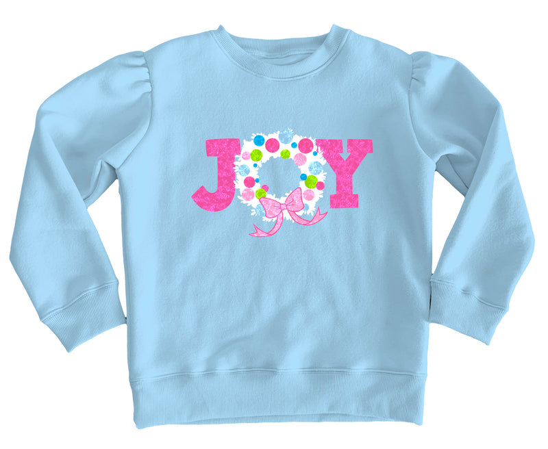 A light blue long-sleeve sweatshirt with a pink and white 'JOY' graphic on the chest, featuring a floral wreath design inside the 'O' and a pink bow.