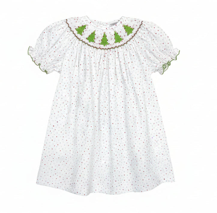 A toddler girl's white dress with tiny red polka dots and green embroidered Christmas tree motifs across the yoke, hanging on a clear plastic hanger in a retail store.