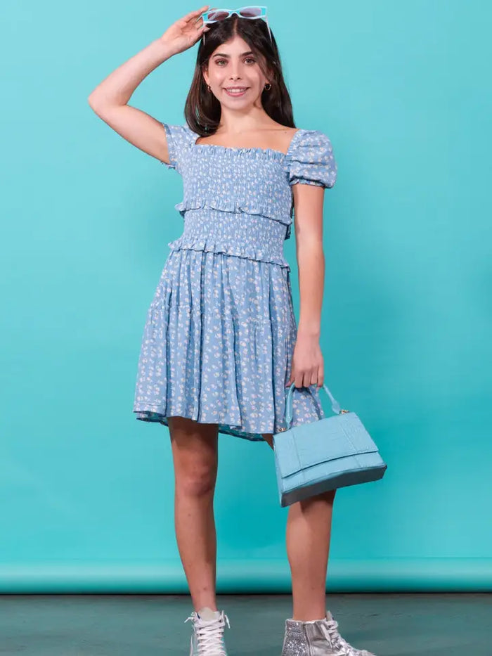 Woman in a blue patterned dress holding a matching handbag against a teal background