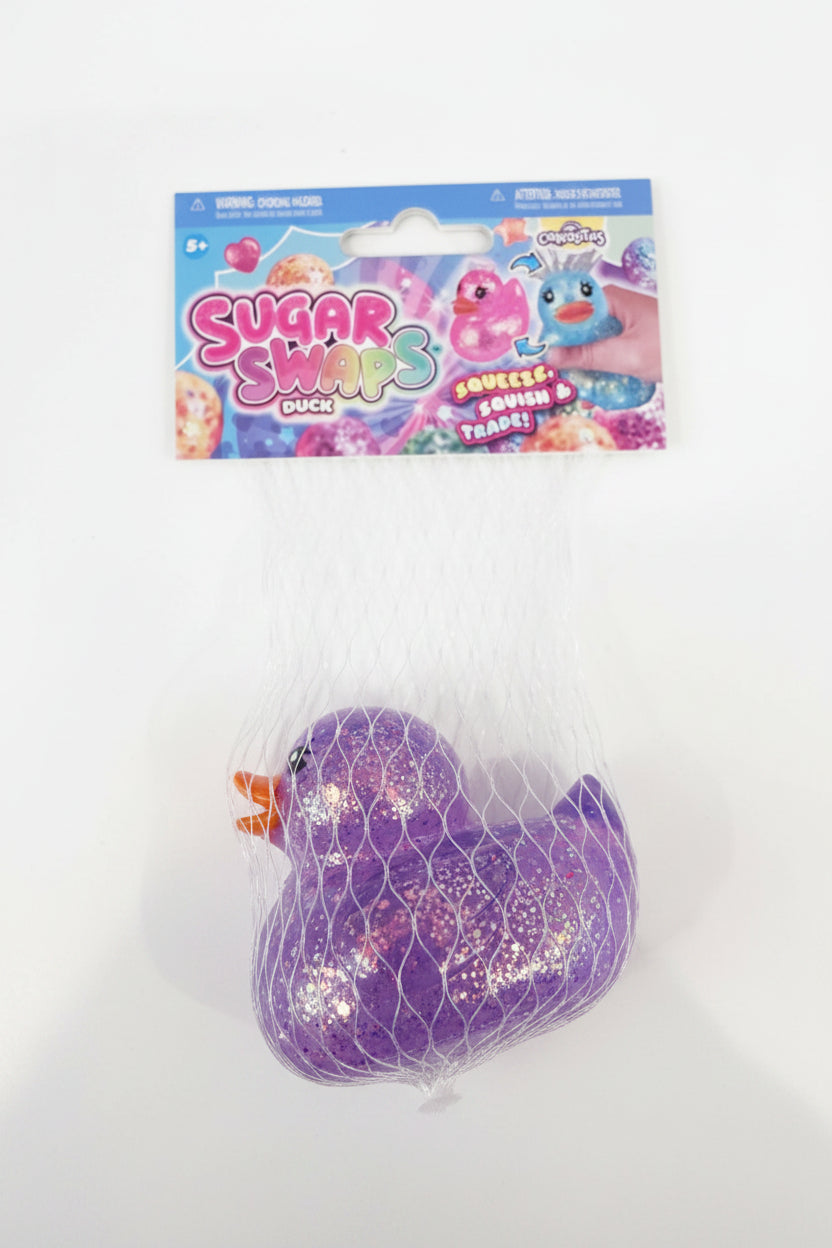 A purple glittery squeaky duck toy in a clear mesh bag with its original Sugar Swaps Duck packaging card attached at the top, placed on a light gray surface.