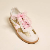 White and gold sneaker with pink floral laces on a beige background