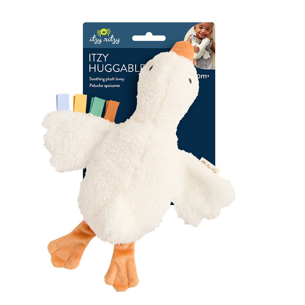 Itzy Huggable plush duck toy with a soft cream body, orange beak and feet, and small colorful fabric tabs on the wing, shown on its branded retail card against a white background.