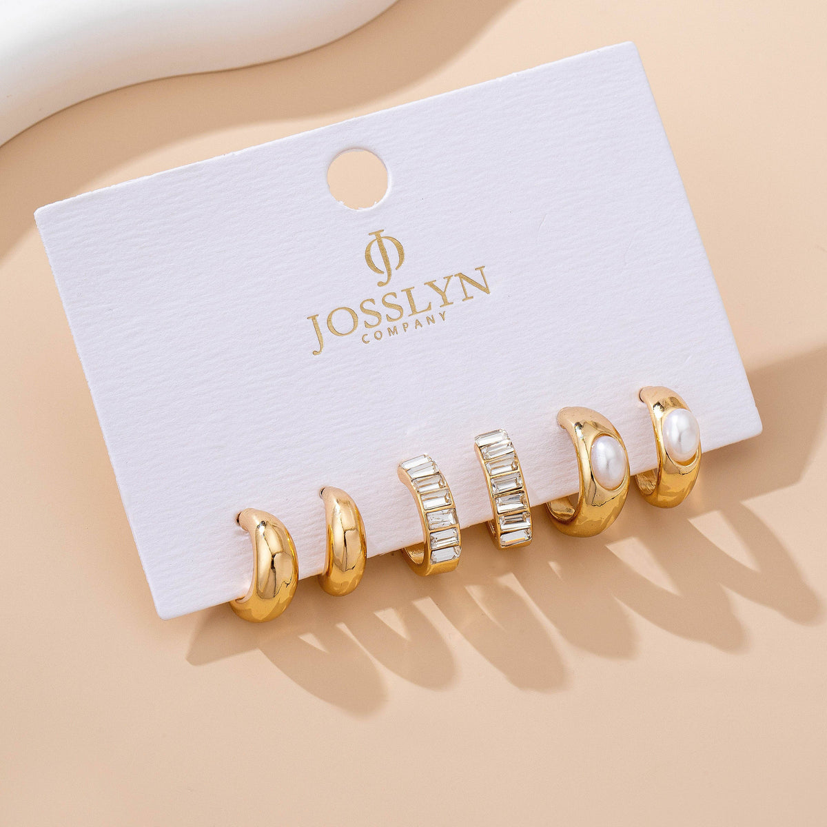 Set of gold hoop earrings with pearls on a JOSSLYN Company card against a beige background