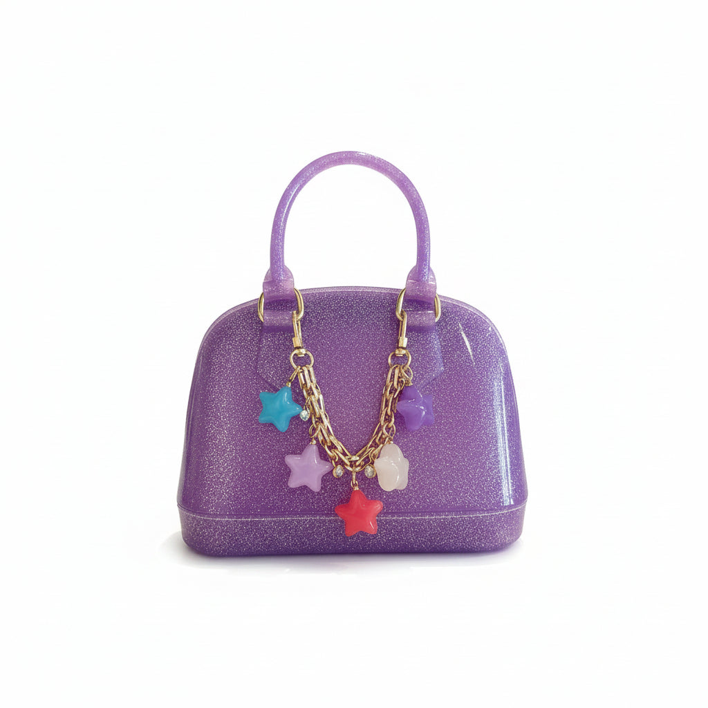 A small glittery purple handbag with a gold-tone chain charm decorated with colorful star and oval charms, displayed on a white surface with a clothing store background.