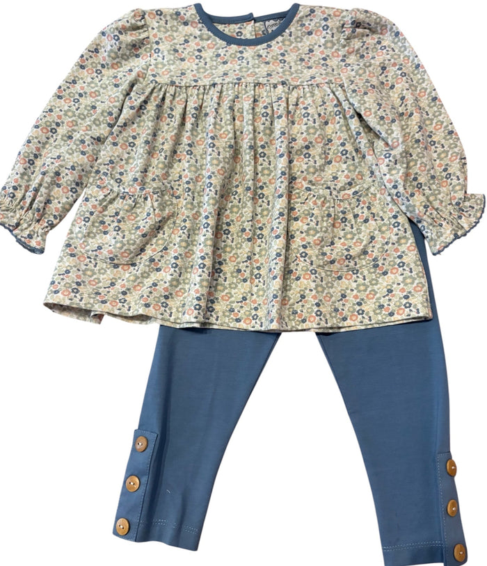 A toddler girl's two-piece outfit featuring a long-sleeve cream-colored blouse with a dense multicolor floral print and blue trim, paired with blue pants that have decorative gold buttons at the cuffs.