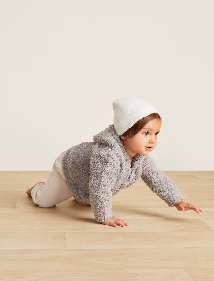 Baby in a gray fleece outfit and white hat crawling on a wooden floor.