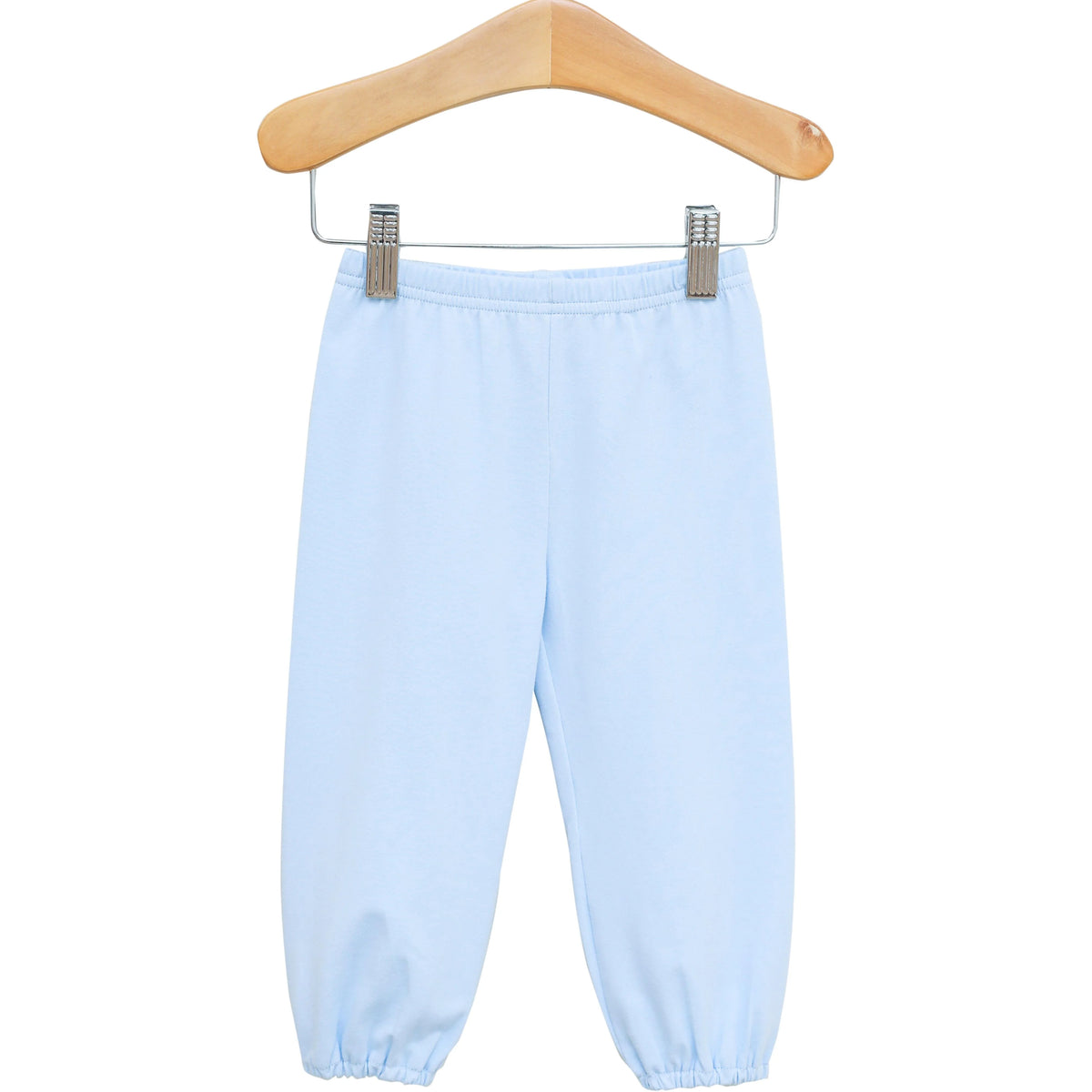 Light blue pants with an elastic waistband and elastic cuffs, hanging from a wooden hanger with metal clips against a plain white background.