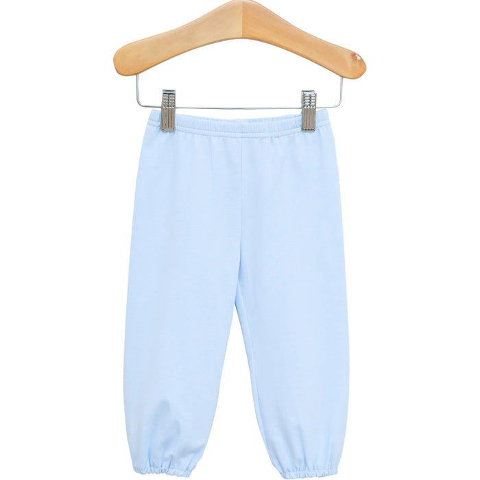 Light blue pants with an elastic waistband and elastic cuffs, hanging from a wooden hanger with metal clips against a plain white background.