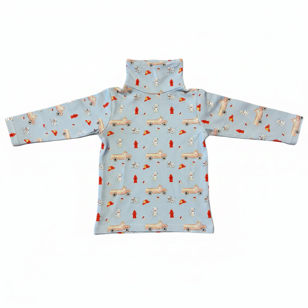 A light blue long-sleeve turtleneck top with a repeating pattern of fire trucks, Dalmatian dogs, and red fire hydrants, laid flat on a white background.