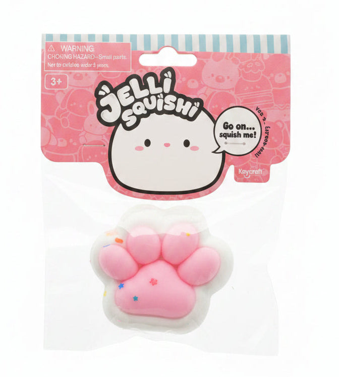 A pink and white Jelliqushii jelly paw toy in its original retail packaging, placed on a light-colored wooden surface.