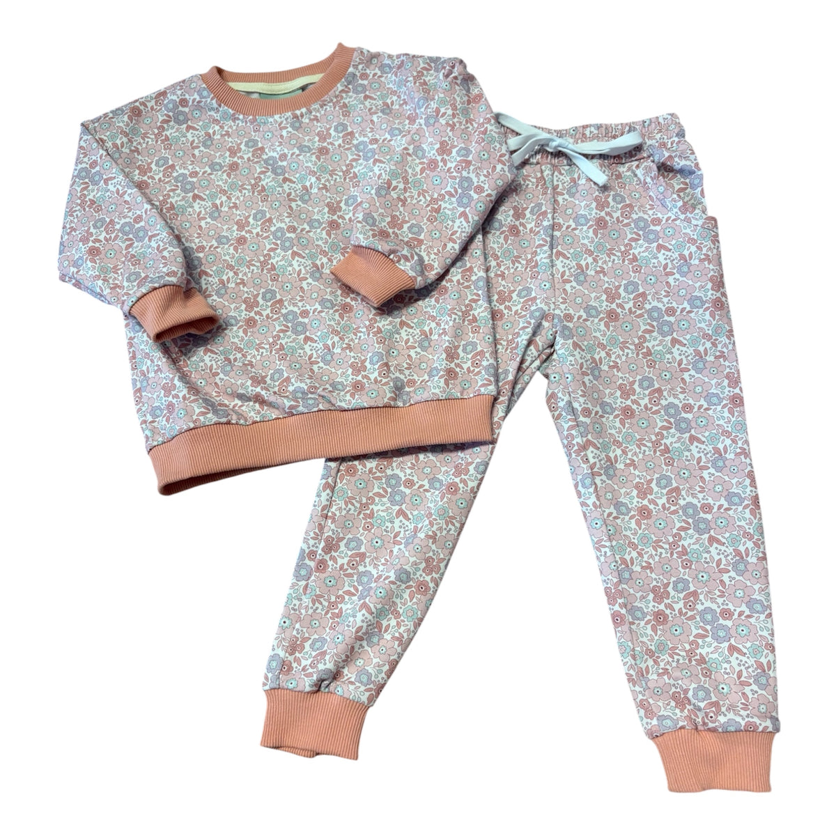 A two-piece kids' loungewear set featuring a long-sleeve sweatshirt and matching jogger pants with an all-over floral pattern in muted blue, pink, and brown tones, finished with solid tan ribbed cuffs and hem.