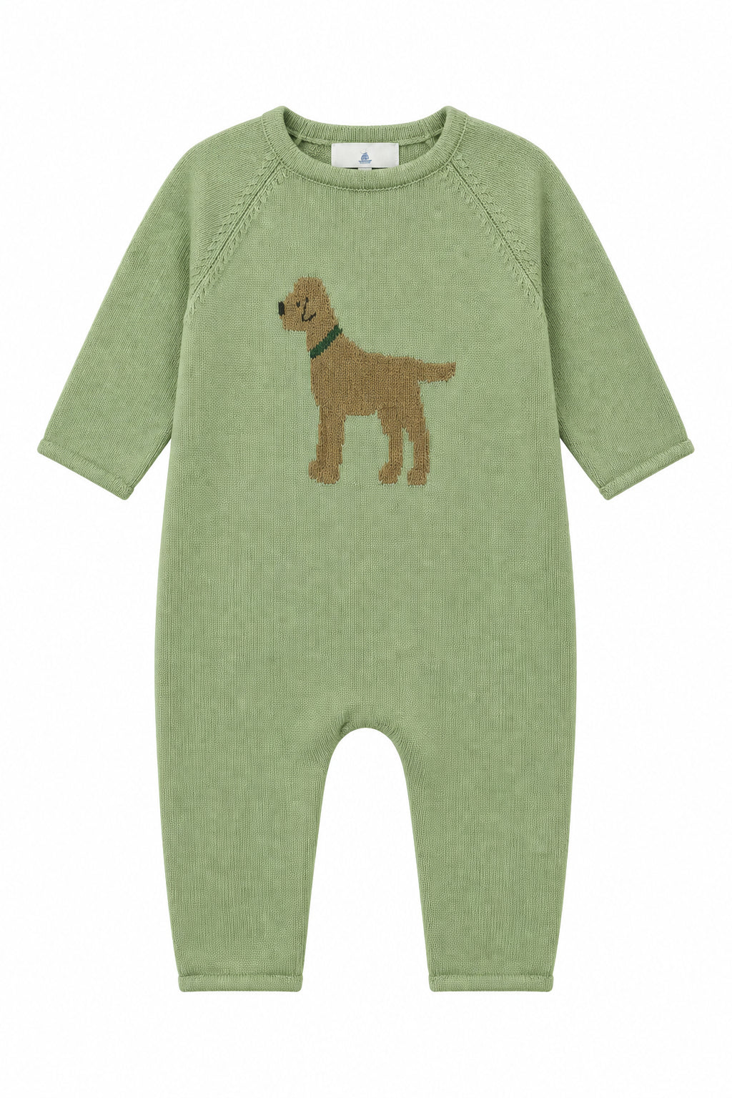 A sage green baby knit romper with a brown dog graphic on the chest, hanging on a hanger in a retail store setting with shoe boxes stacked on shelves.