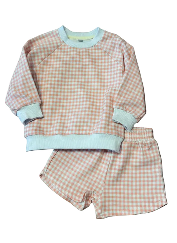 A baby two-piece outfit set consisting of a long-sleeve sweatshirt and matching shorts in a light peach and white gingham check pattern, with solid pale blue ribbed trim on the collar, cuffs, and hem, laid flat on a gray surface.