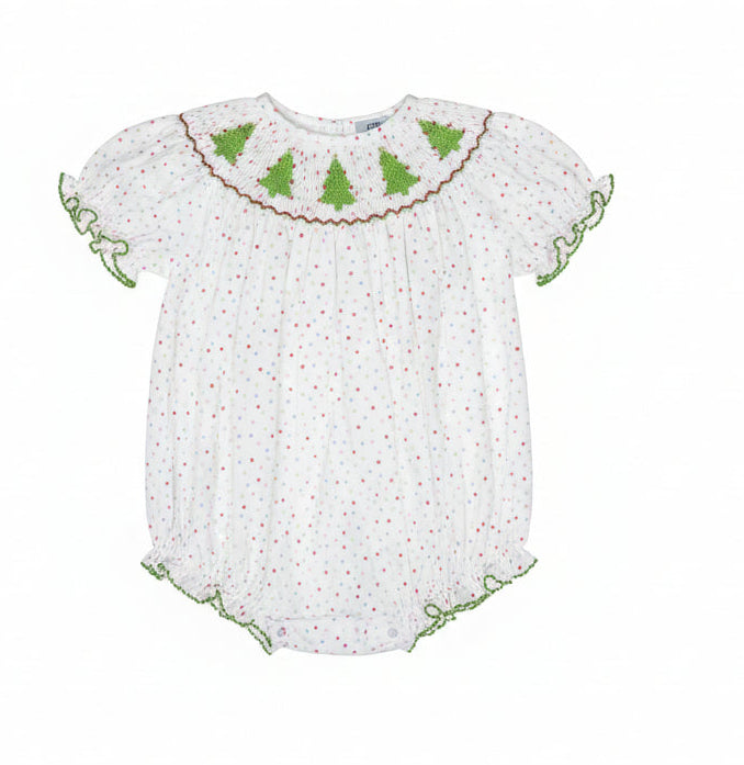A white baby smocked blouse with red polka dots, green trim, and green embroidered Christmas tree motifs across the yoke, hanging on a clear hanger in a retail store.