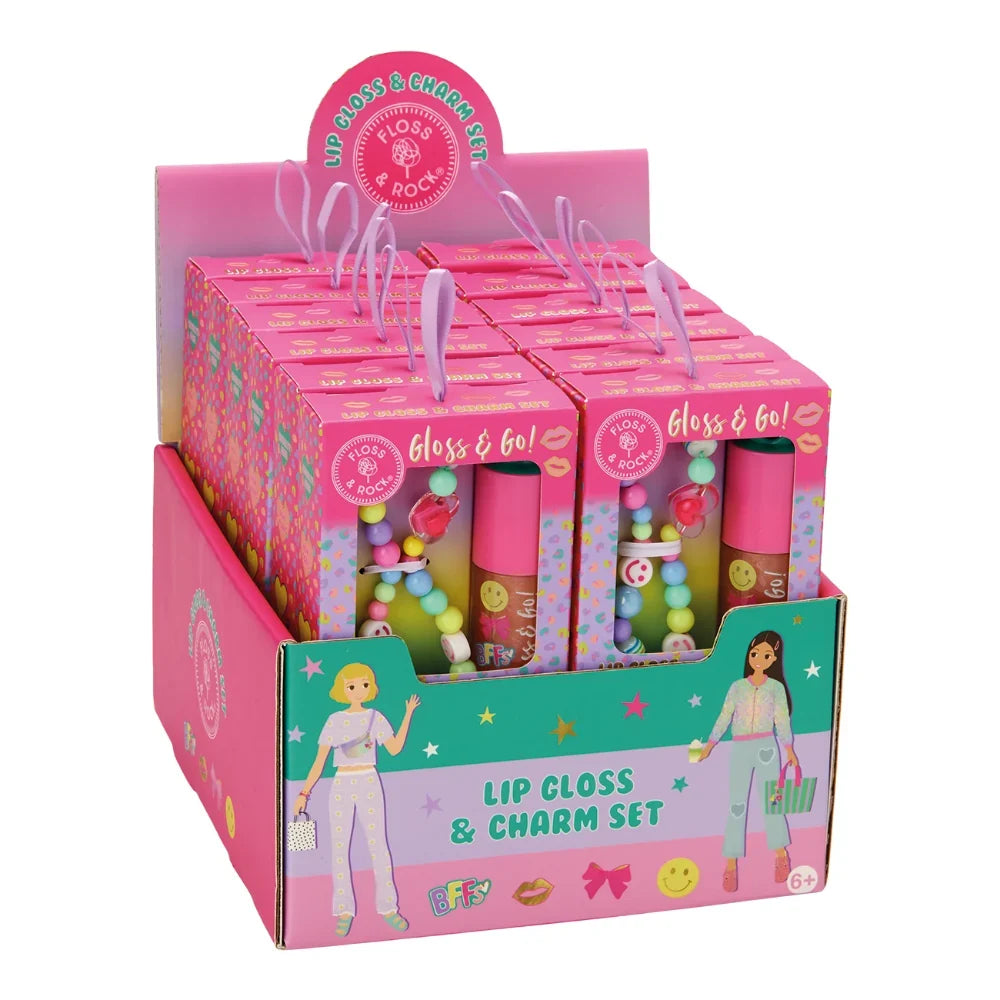 A pink retail display box containing multiple lip gloss and charm sets. Each set includes a pink tube of gloss and a small charm with pastel beads, shown in a branded pink box with cartoon illustrations and the text 'Lip Gloss & Charm Set'.
