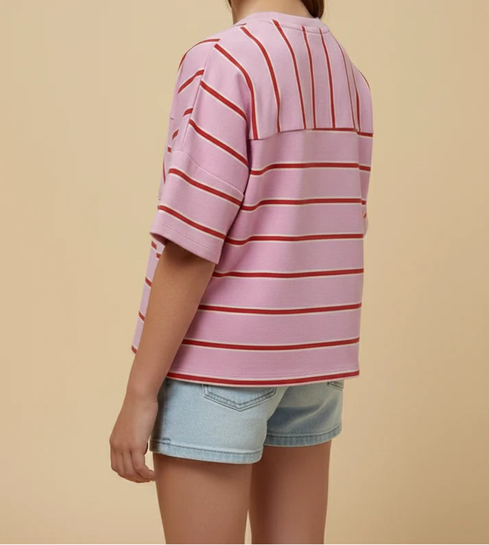 Young girl wearing a pink and red striped shirt with denim shorts on a beige background