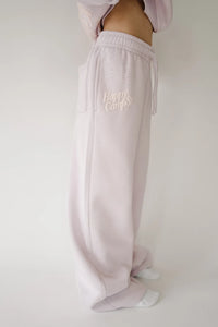 A person wearing light pink sweatpants with a drawstring waist and 'Happy Camp3r' embroidered on the thigh, shown against a plain light background.