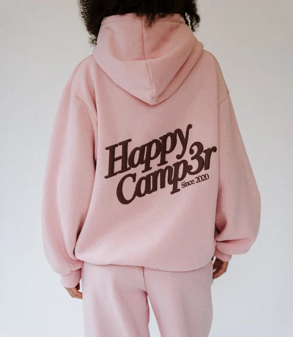 A person shown from the back wearing a light pink hoodie and matching sweatpants, with a large dark brown graphic reading 'Happy Camp3r Since 2020' across the back.
