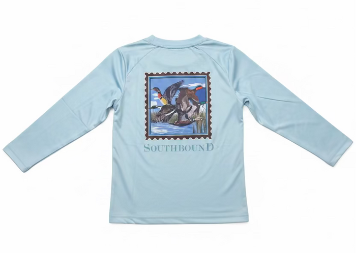 A light blue long-sleeve shirt with a large duck hunting graphic on the back, held up by a hand. The graphic features a stamp-like border with ducks in a marsh and the word 'SOUTHBOUND' printed below.