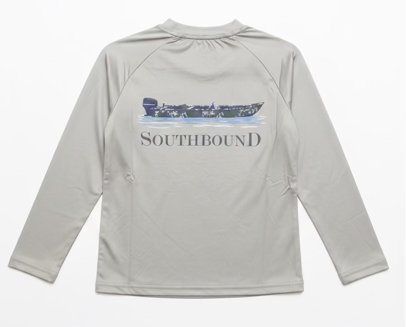 A light gray long-sleeve raglan shirt hanging on a clear hanger, showing the back with a dark blue boat graphic and the word SOUTHBOUND printed across it. A person's hand with purple nail polish and gold bracelets is holding the collar.