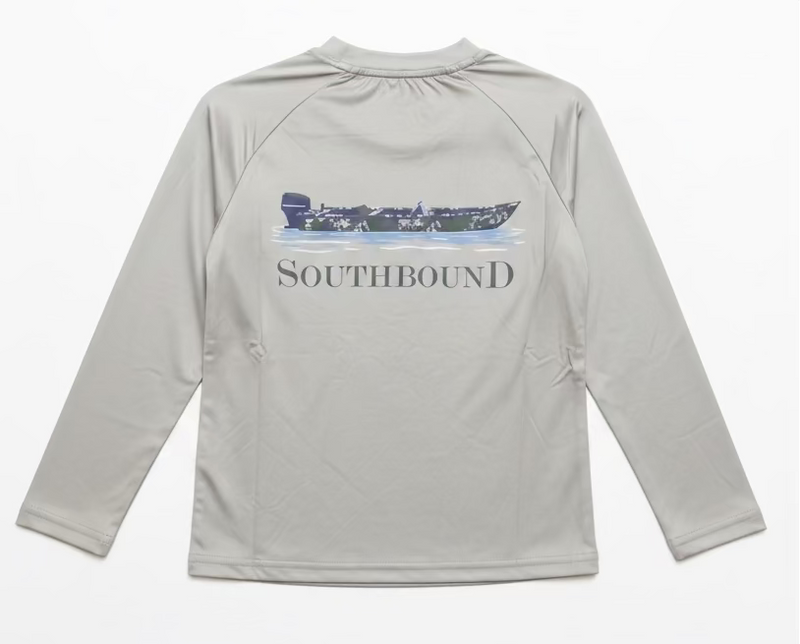 A light gray long-sleeve raglan shirt hanging on a clear hanger, showing the back with a dark blue boat graphic and the word SOUTHBOUND printed across it. A person's hand with purple nail polish and gold bracelets is holding the collar.