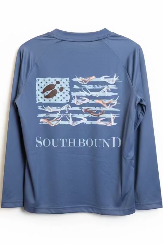 A blue long-sleeve performance shirt with a graphic print of a paw-print American flag and the word SOUTHBOUND, held up on a hanger in an indoor setting.