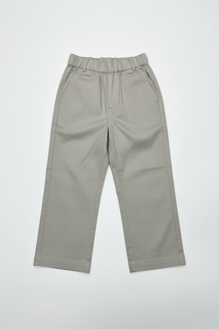 A pair of light beige wide-leg cropped pants hanging on a clear plastic hanger from a store display shelf, with shoe boxes stacked behind them.