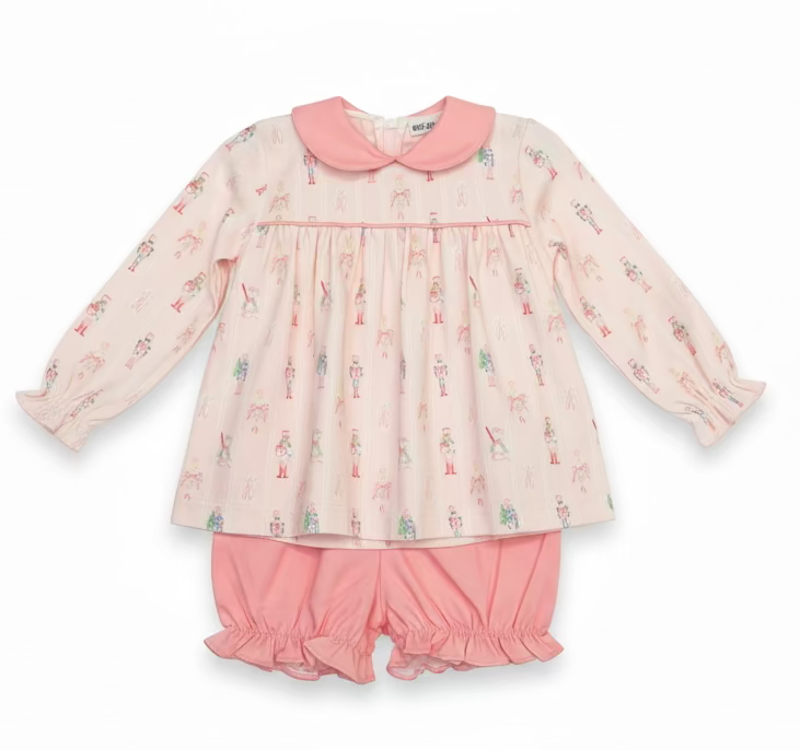 A children's two-piece pajama set hanging on a hanger in a retail or storage area. The set includes a long-sleeve top with a pink Peter Pan collar and a pink and white nutcracker print, paired with matching pink ruffled shorts.