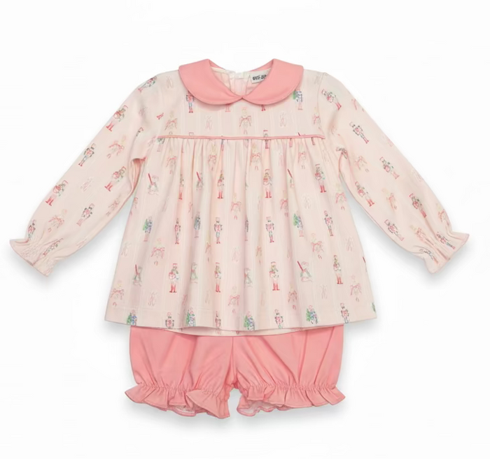 A children's two-piece pajama set hanging on a hanger in a retail or storage area. The set includes a long-sleeve top with a pink Peter Pan collar and a pink and white nutcracker print, paired with matching pink ruffled shorts.