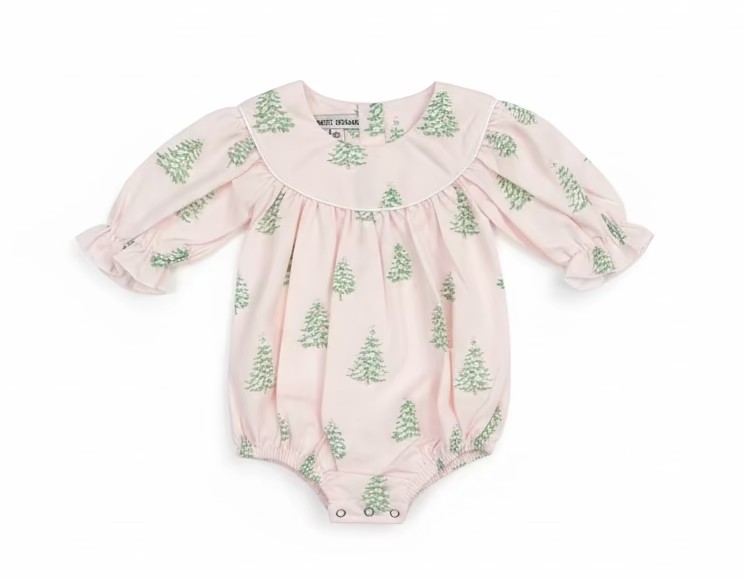 A baby romper in a pale pink fabric with a green pine tree pattern, hanging on a clear plastic hanger on a store shelf.