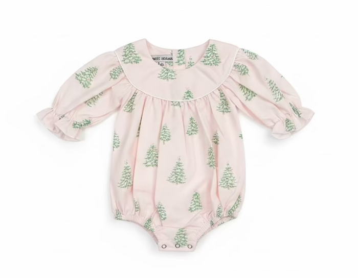 A baby romper in a pale pink fabric with a green pine tree pattern, hanging on a clear plastic hanger on a store shelf.