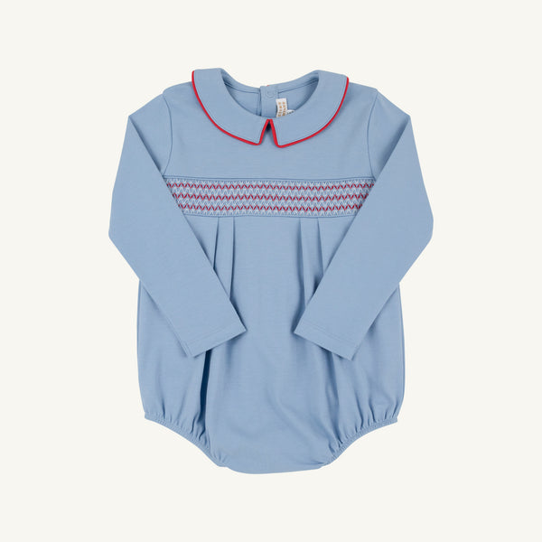 A light blue long-sleeve baby romper with a decorative zigzag smocked chest band in red and white, and a red-trimmed Peter Pan collar, shown flat on a light cream background.