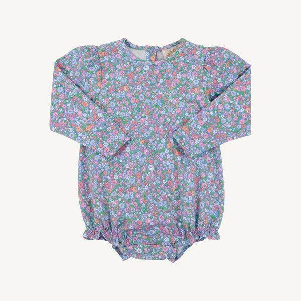 A long-sleeve baby bodysuit with a dense multicolor floral print on a light blue-gray base, featuring elasticized cuffs and a ruffled snap crotch, laid flat against a light cream background.