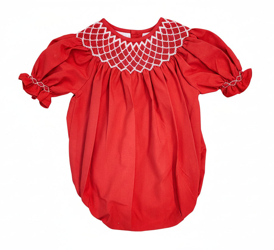 A baby girl's short-sleeve smocked blouse in terracotta red, featuring a white embroidered net pattern around the collar and matching white embroidery on the sleeve cuffs, shown against a plain white background.