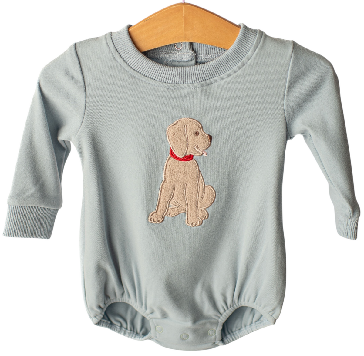 A baby long-sleeve romper in a dusty light blue-gray color, featuring an embroidered puppy with a red collar on the chest. The romper is displayed on a wooden hanger against a solid white background.
