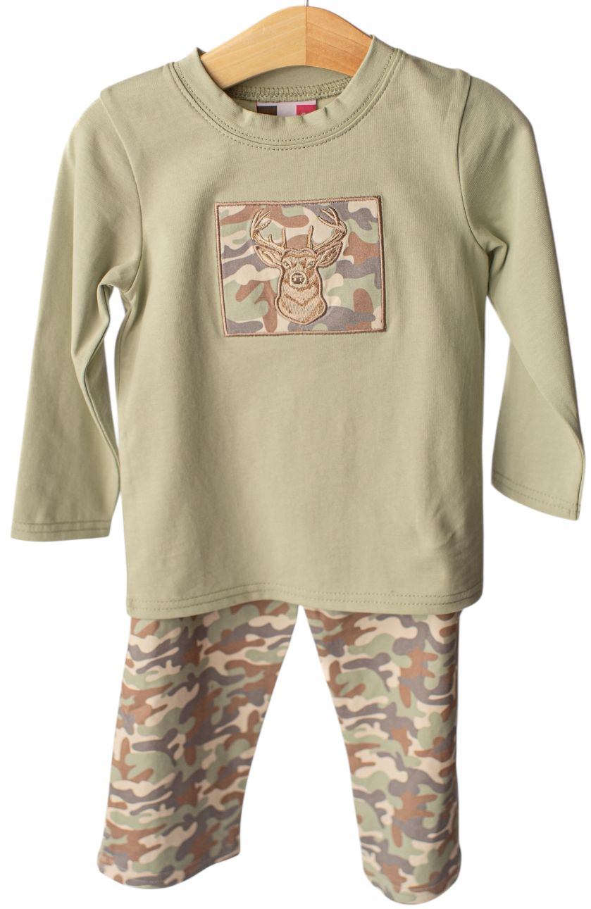 A children's two-piece pajama set hanging on a wooden hanger against a white background. The long-sleeve top is a light khaki color with a rectangular camouflage patch on the chest, and the pants feature a classic camouflage pattern in shades of green, brown, and beige.