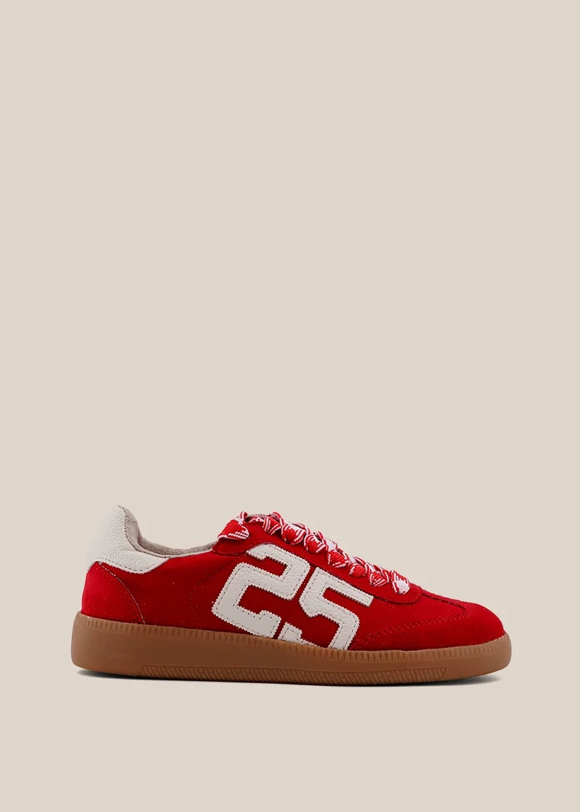 A red suede sneaker with a large white '25' on the side, red laces, and a brown gum sole, shown against a solid beige background.