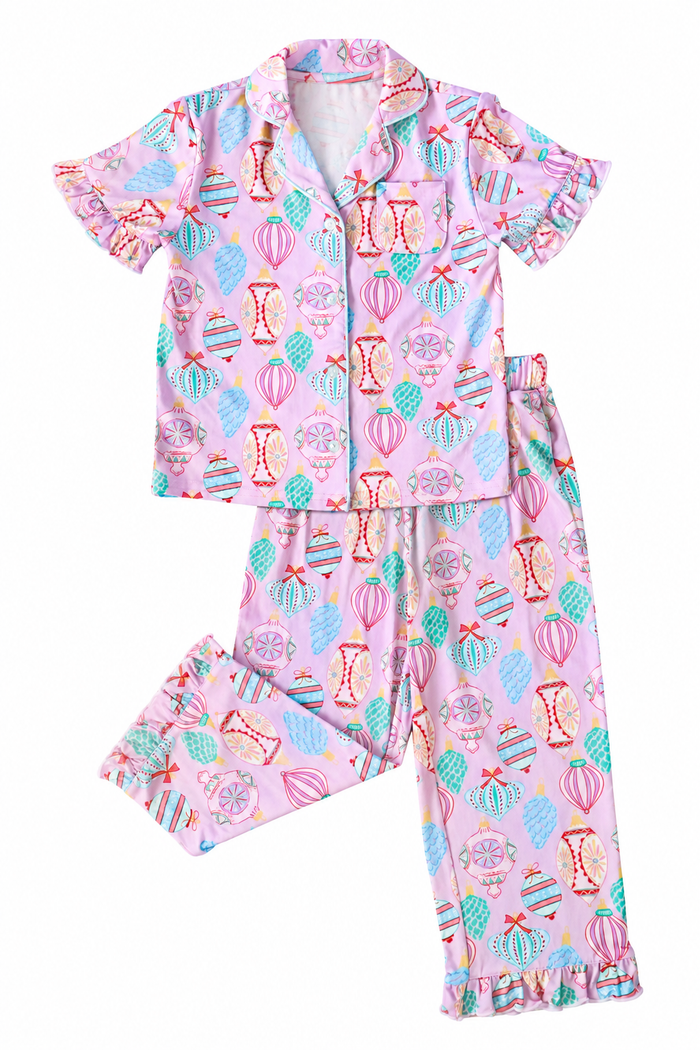 A two-piece girls' pajama set featuring a short-sleeve button-up top and matching pants, both in light pink with a colorful pattern of hot air balloons, hourglasses, and floral motifs.