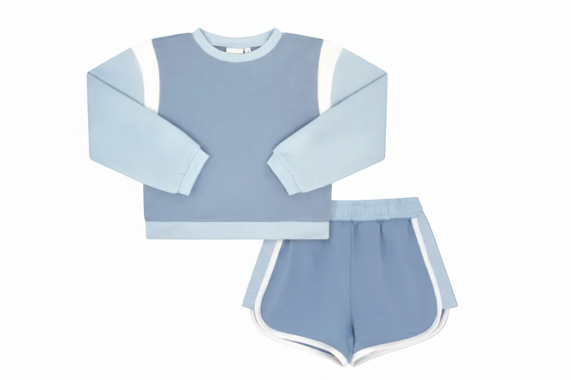 A two-piece children's outfit set in light blue, featuring a long-sleeve top with white contrast panels on the shoulders and sleeves, and matching shorts with white side trim.