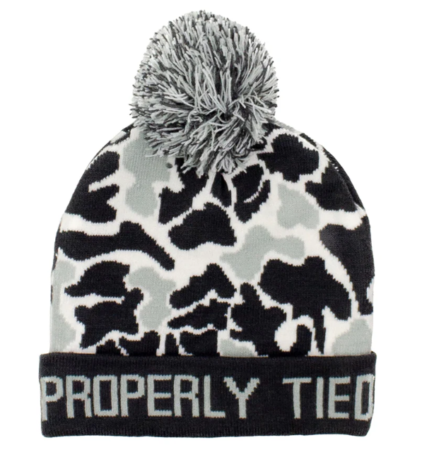 A knit pom-pom beanie hat featuring a black, gray, and off-white camouflage pattern, with a black cuff displaying the white text 'PROPERLY TIED' and a gray and black pom-pom on top.