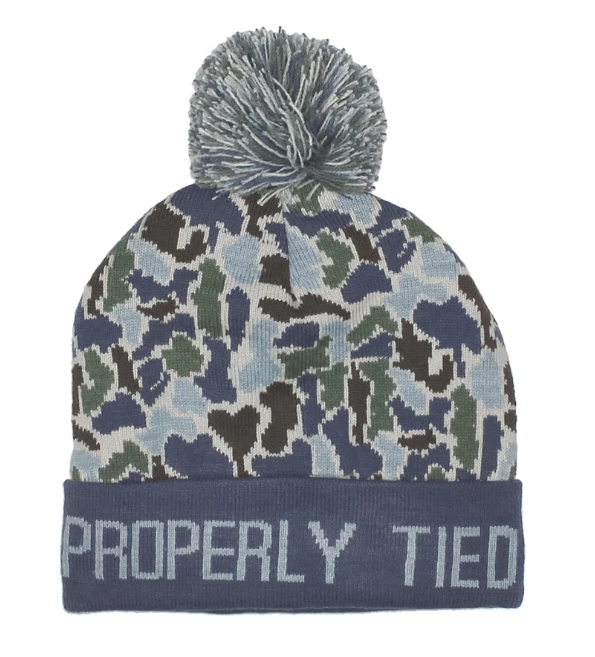 A navy blue knit beanie with a camouflage pattern in navy, green, and light blue, featuring a gray pom-pom on top and 'PROPERLY TIED' embroidered in white on the cuff.