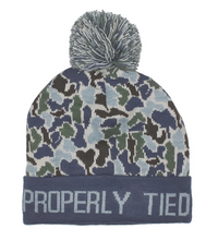 A navy blue knit beanie with a camouflage pattern in navy, green, and light blue, featuring a gray pom-pom on top and 'PROPERLY TIED' embroidered in white on the cuff.