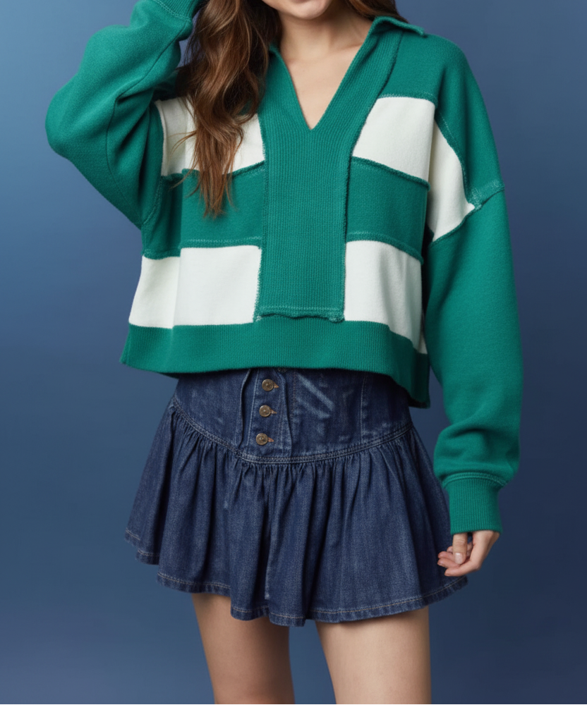 A young woman wearing a green and white color-block knit cardigan sweater and a dark blue denim pleated mini skirt, posing against a textured blue studio background.