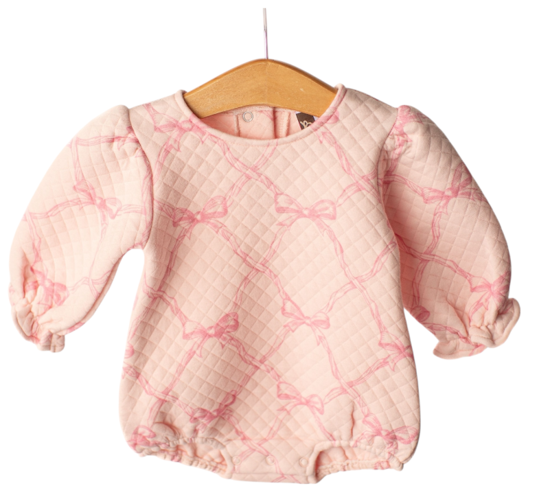A baby long-sleeve quilted romper in light pink with a darker pink bow lattice pattern, hanging on a wooden hanger against a white background.