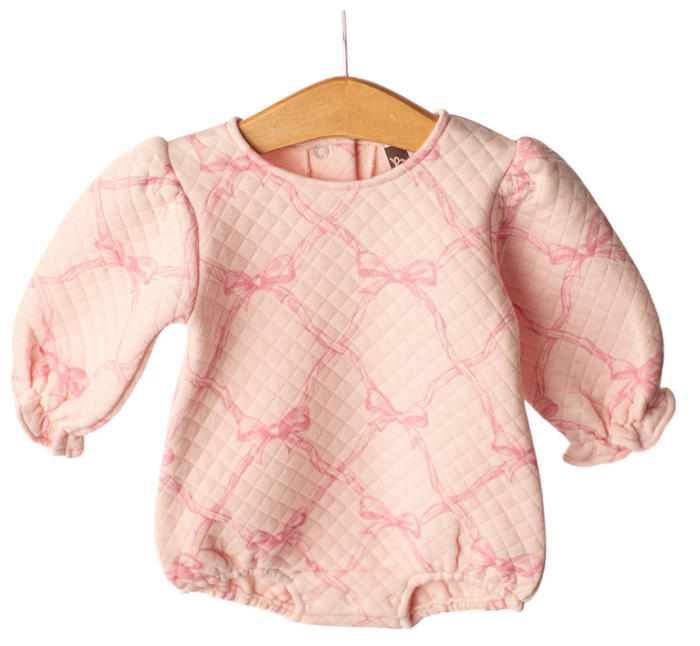 A baby long-sleeve quilted romper in light pink with a darker pink bow lattice pattern, hanging on a wooden hanger against a white background.