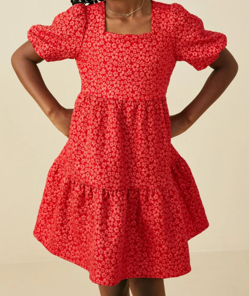 A red tiered dress with a small white floral pattern, featuring puff sleeves and a square neckline, shown on a model against a plain beige background.